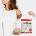 Woman lifting her white blazer sleeve to show a tan Garment Guard underarm shield applied inside, with the retail package and a stack of shields shown beside it