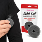 Hand holding a gray Skid Out stain eraser sponge next to a deodorant mark on a black shirt sleeve, with the 2-pack retail package shown alongside